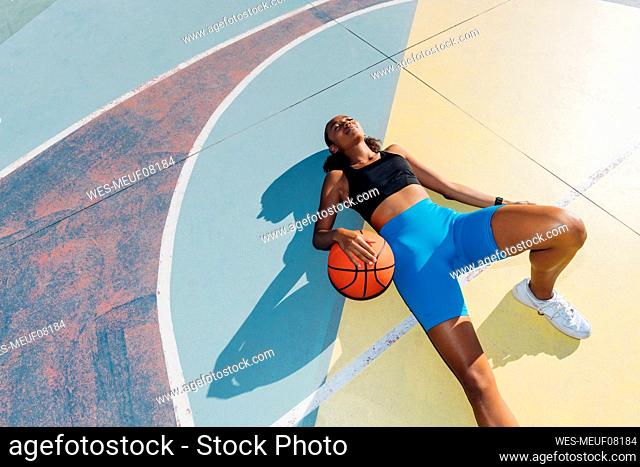 Young sportswoman relaxing with ball lying on basketball court