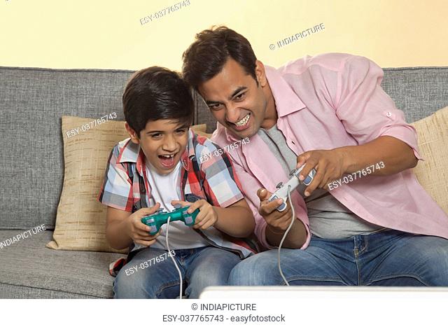 Father and son sitting on sofa playing video games
