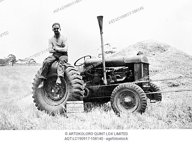 Negative - Yendon, Victoria, 1939, Man sitting with crossed arms on the wheel of a Fordson tractor that has a conveyor belt attached to it