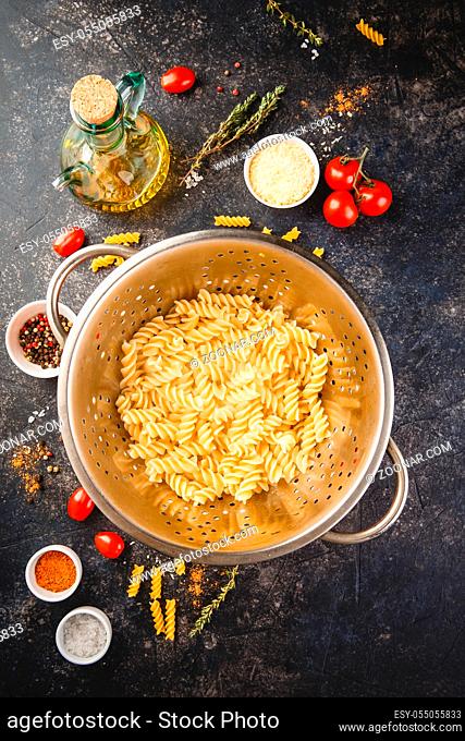 Fusilli pasta in stainless steel colander and ingredients over dark background. Top view or flat-lay