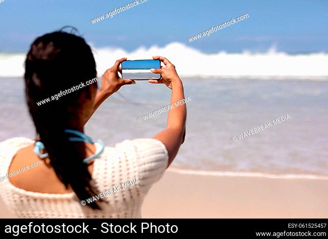 African american woman on a beach taking photo of the sea with smartphone