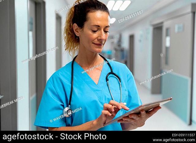 Portrait of mixed race female doctor standing in hospital corridor using tablet