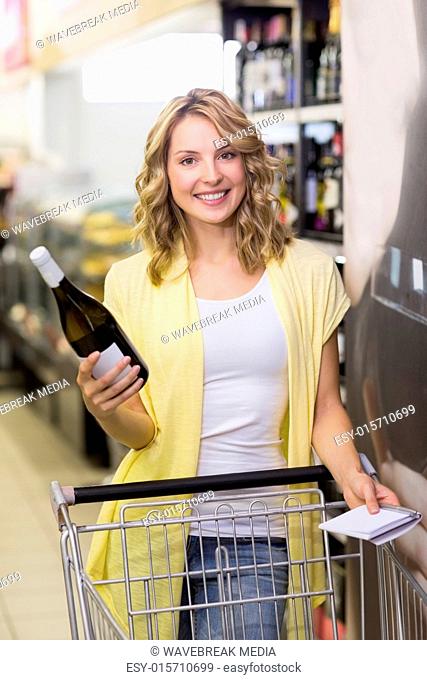 Portrait of a smiling pretty blonde woman having a notepad and wine bottle in her hands