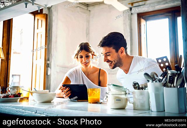 Young couple watching tablet while having breakfast at home