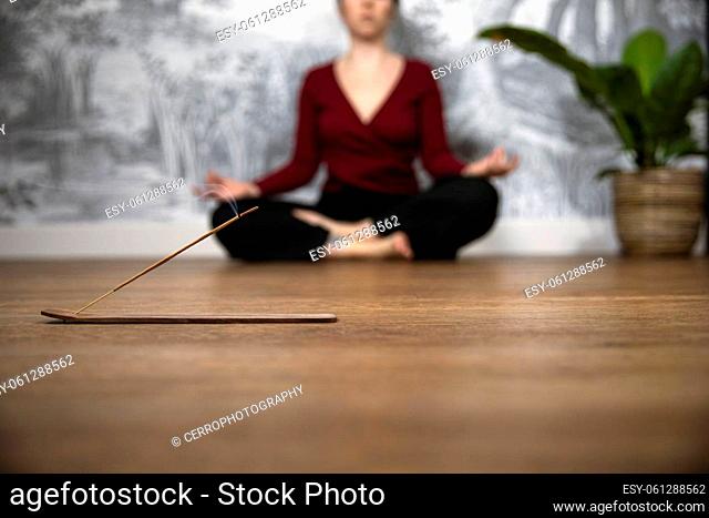 Mindful woman meditating at home with burning incense sticks, siting in lotus pose. Holding hands in lap with palms facing upwards