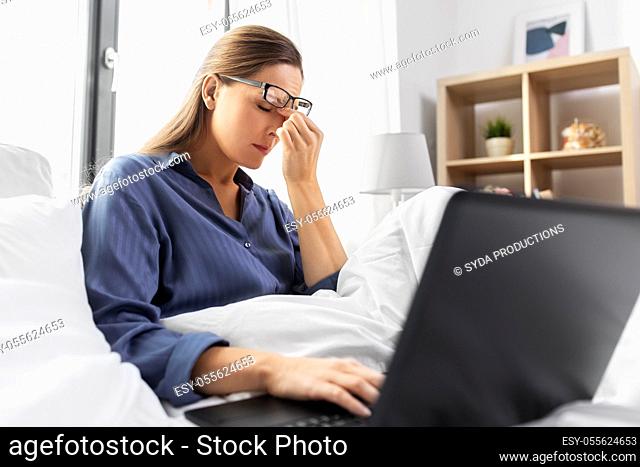 tired woman in glasses with laptop in bed at home
