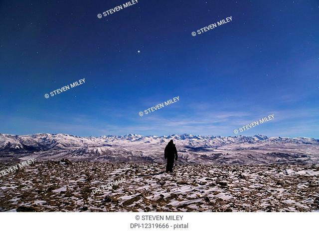 A man looks toward the Alaska Range from the top of Donnelly Dome on a moonlit night (the bright object in the sky is Jupiter); Alaska, United States of America