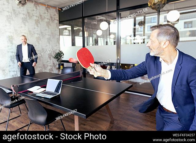 Male professionals playing table tennis at office