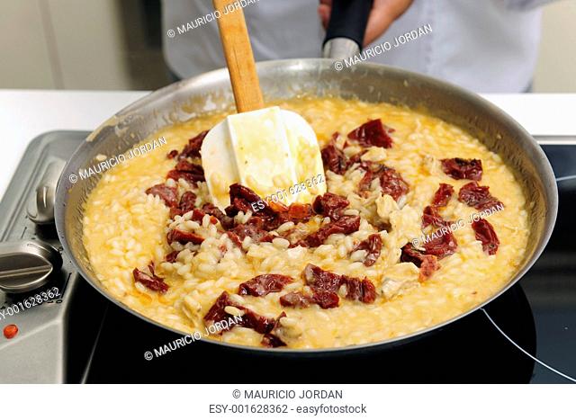 Chef cooking risotto with dried tomato stirring