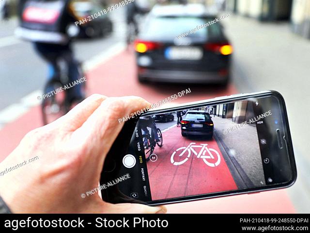16 April 2021, North Rhine-Westphalia, Cologne: ILLUSTRATION - A smartphone shows a picture of a car stopping in a bike lane