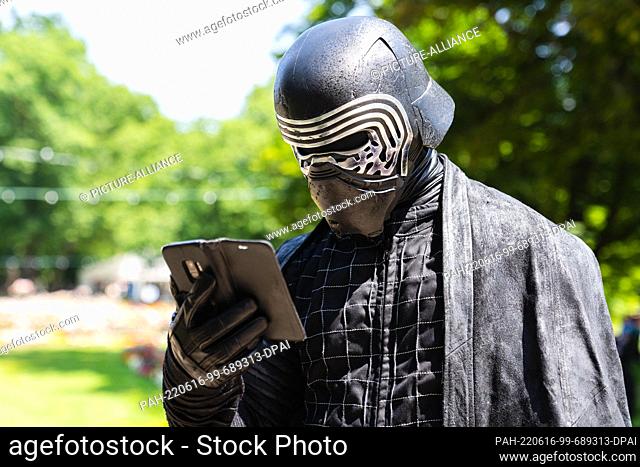 16 June 2022, Bavaria, Erlangen: Cosplayer Frank, here in his costume as the Star Wars character Kylo Ren, looks at his smartphone while visiting the Comic...