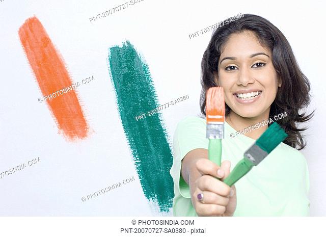 Portrait of a young woman holding paintbrushes and smiling