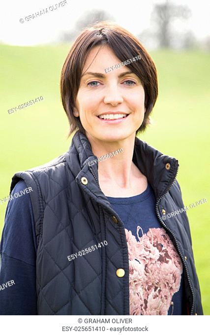 Head and shoulder portrait of a woman looking at the camera, she is outdoors. A grassy area can be seen behind her, She smiles