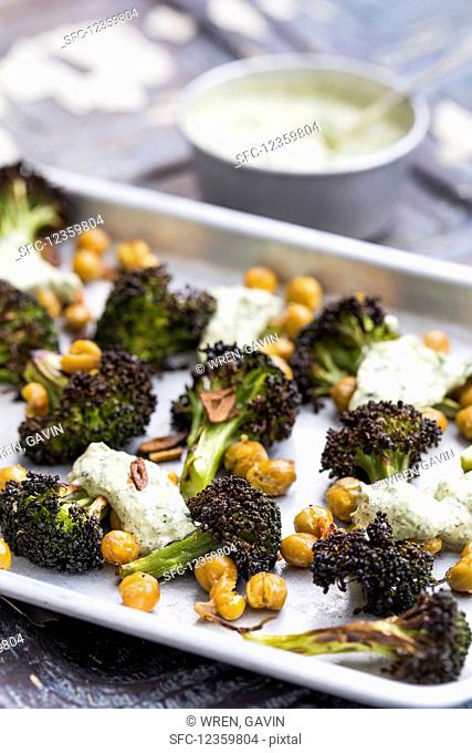 Aluminium tray with roasted broccoli florets and chickpeas, topped with garlic herb yoghurt, on an aged metal background