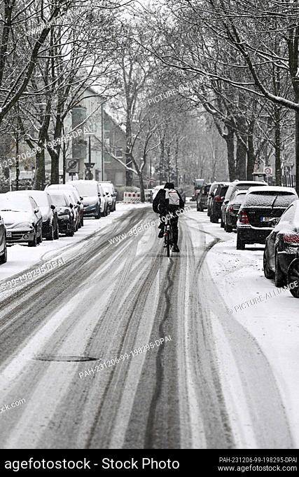 06 December 2023, Berlin: A cyclist rides on a snow-covered road in Karlshorst on which the tracks of cars can be seen. There is a risk of black ice due to...