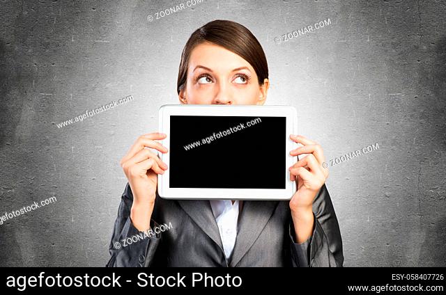 Businesswoman holding tablet computer with blank screen. Beautiful woman in business suit show tablet PC near her face. Corporate businessperson on grey wall...