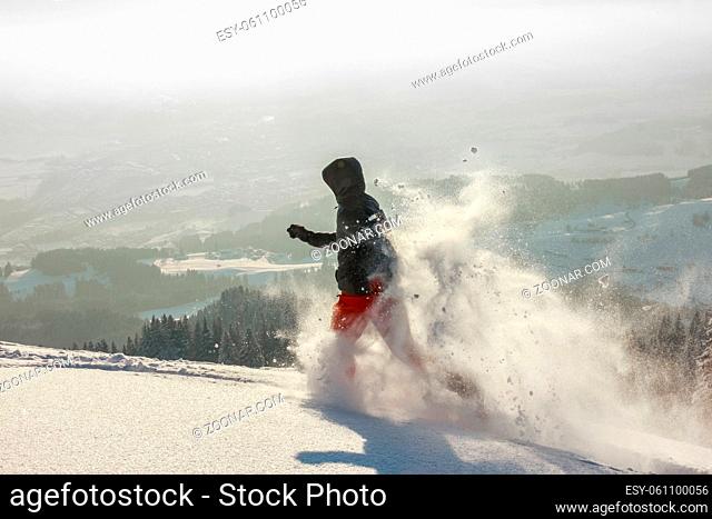 Happy Man with hood running in deep powder snow with snowshoes on a Mountain. Snow is spraying and splashing