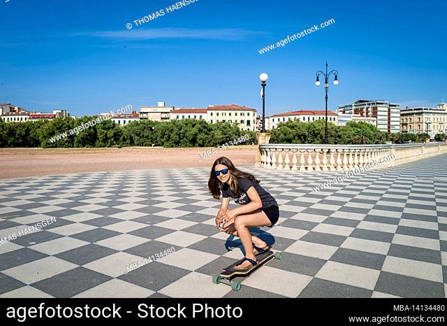 skater girl skating and jumping on terrazza mascagni in livorno, italy. its a wide sinuous belvedere toward the sea with a paving surface of 8700 sqm like a...