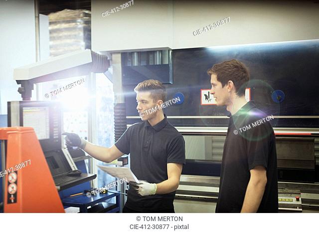 Worker training trainee at machinery control panel in steel factory