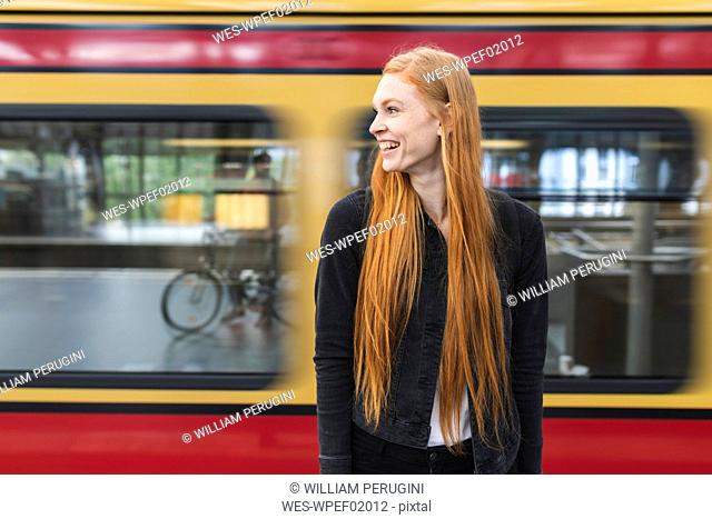 Laughing redheaded young woman waiting at platform, Berlin, Germany