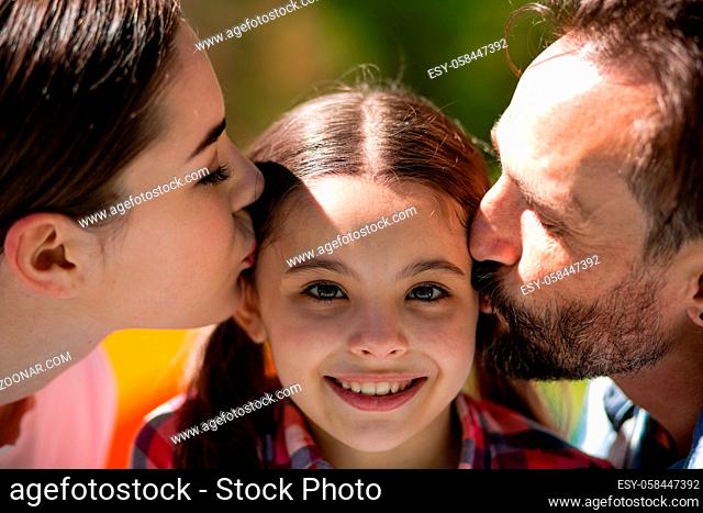 Happy Patents Kissing Daughter Cheecks In Summer Park. Spending Time Together. Happy Family Concept