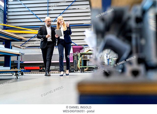 Businessman and businesswoman with tablet walking in factory