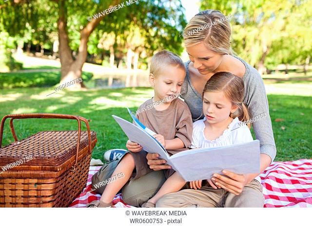 A mother and her kids read a book together in the park