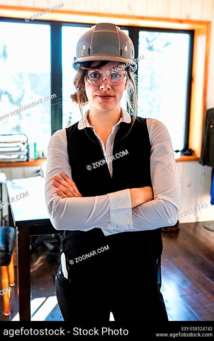 young attractive caucasian woman with crossed arms pose as she wearing classy work clothes with safety grey hard hat and protective eyewear glasses