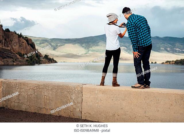 Couple standing on wall beside Dillon Reservoir, looking at camera, rear view, Silverthorne, Colorado, USA