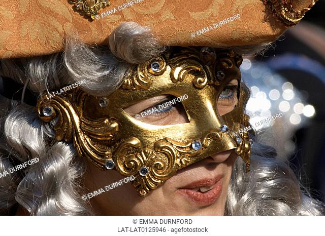 Woman in Venice Carnival outfit, fabric tricorn hat and gold mask with a wig posing in St Marks Square