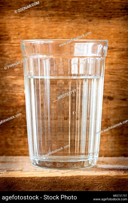 One glass of water, illuminated with natural light, on a wooden plank