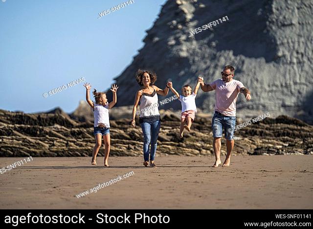Girl watching parents swinging brother while walking at beach