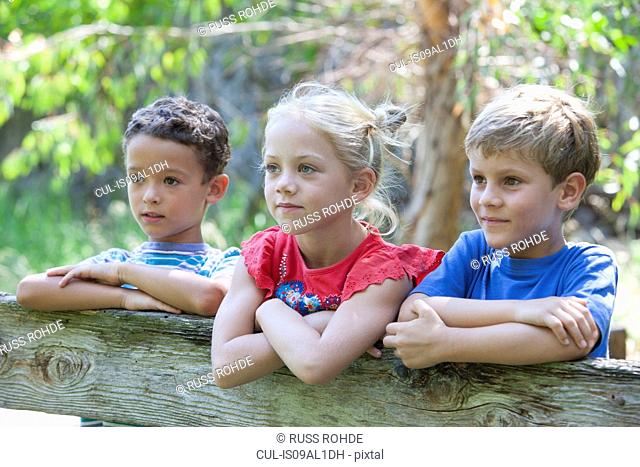 Three children leaning on fence looking away