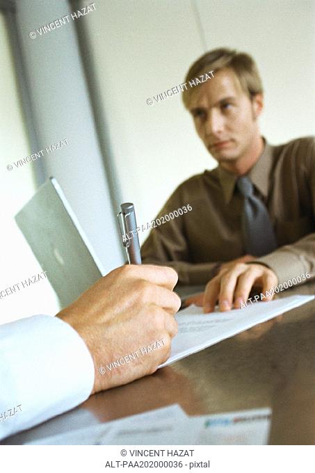 Businessman sitting across from second businessman, close-up of hand writing