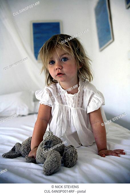 Girl holding teddy bear on bed