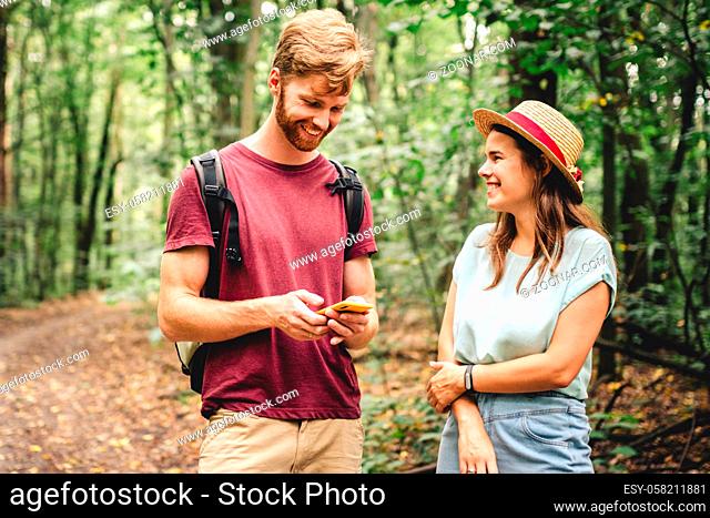 Young caucasian couple uses a smartphone to navigate in the forest. Hiking tourists orientation on the terrain using an online map