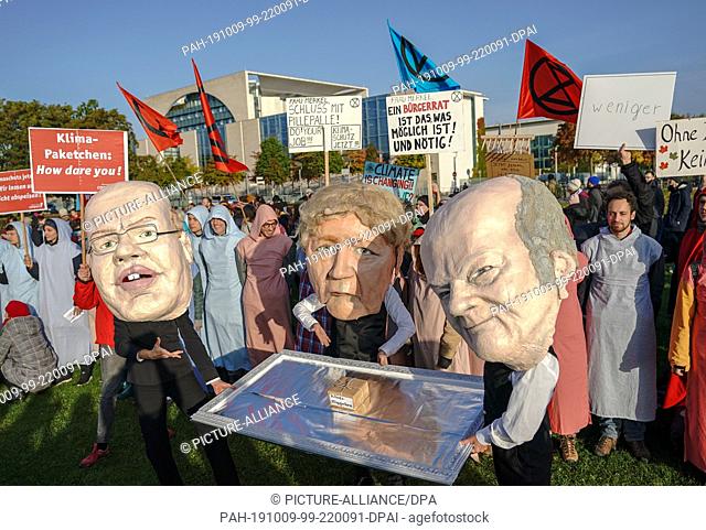 09 October 2019, Berlin: Campact activists are wearing masks, the Economics Minister Altmaier, Chancellor Merkel and Finance Minister Scholz are showing a small...