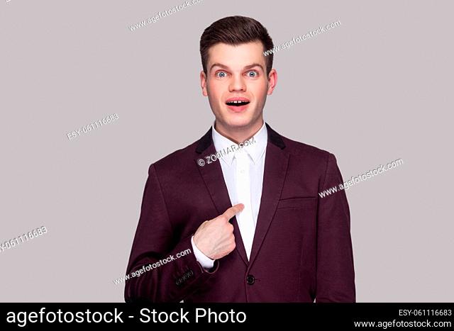 Am I winner?! Portrait of handsome amazed young man in violet suit, white shirt, standing, looking at camera, pointing himself with surprised face and asking