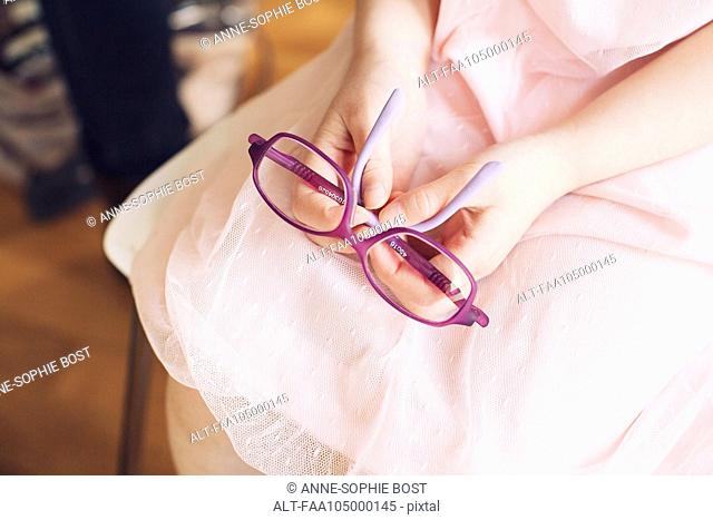 Girl holding pair of glasses on lap, cropped