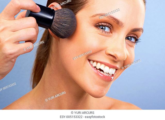 Young woman using a makeup brush to apply her makeup - closeup
