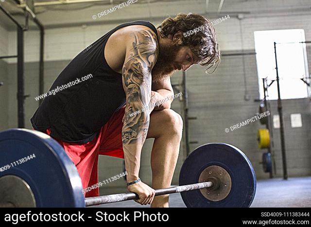 Caucasian athlete crouching at barbell in gym