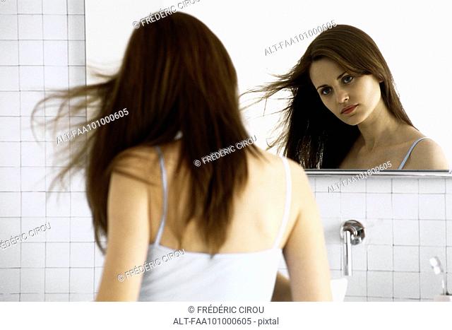 Young woman looking in mirror, drying hair