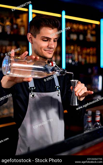 Bartender in apron adds ingredient to cocktail glass