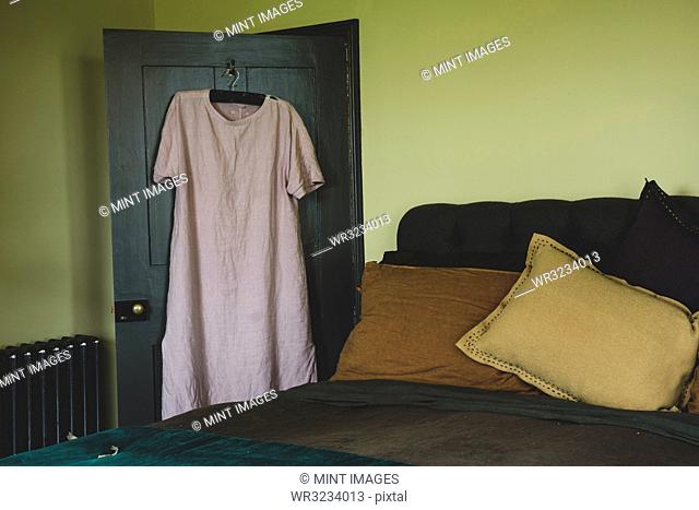 Interior view of bedroom with light green walls, double bed with and pale pink linen nightgown on hanger over door