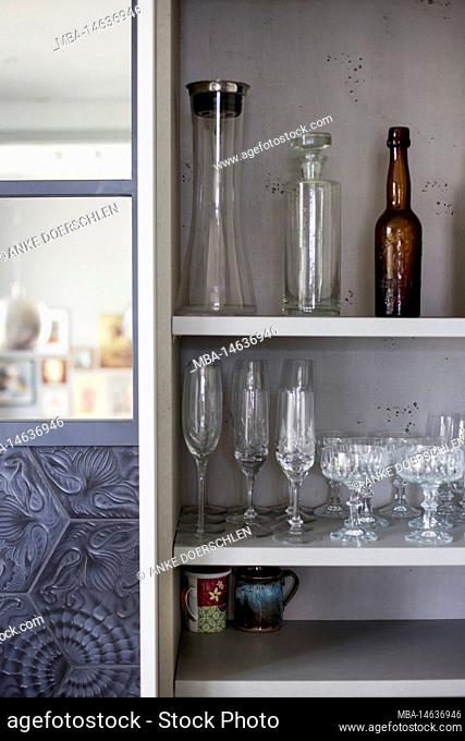 View into an open kitchen cabinet with neatly decorated glasses and bottles