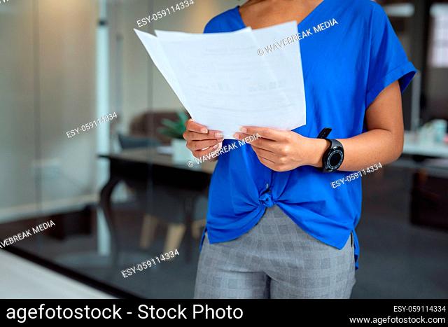 Midsection of african american businesswoman looking at paperwork standing in office
