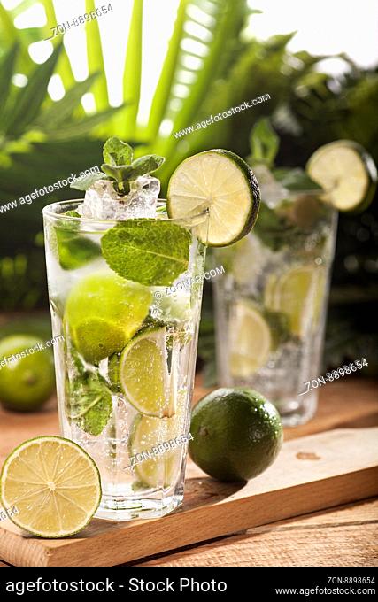 Mojito cocktail on wooden and green tropical leaves background