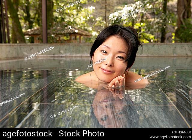 Portrait beautiful young woman soaking in pool at tranquil Onsen