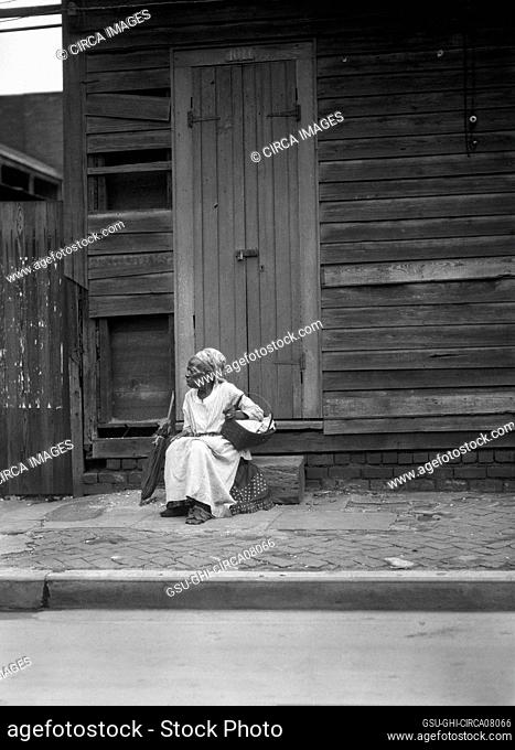 Female Praline Vendor sitting on Steps holding a Basket, New Orleans, Louisiana, USA, Arnold Genthe, 1920's