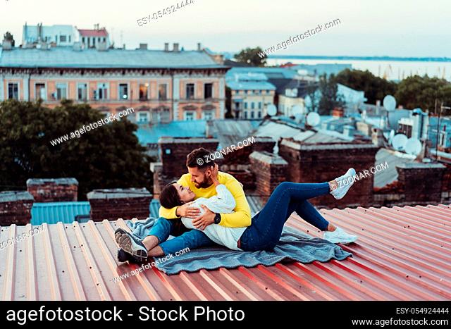 Loving young couple is sitting on the roof of the house. In the background of a big city house